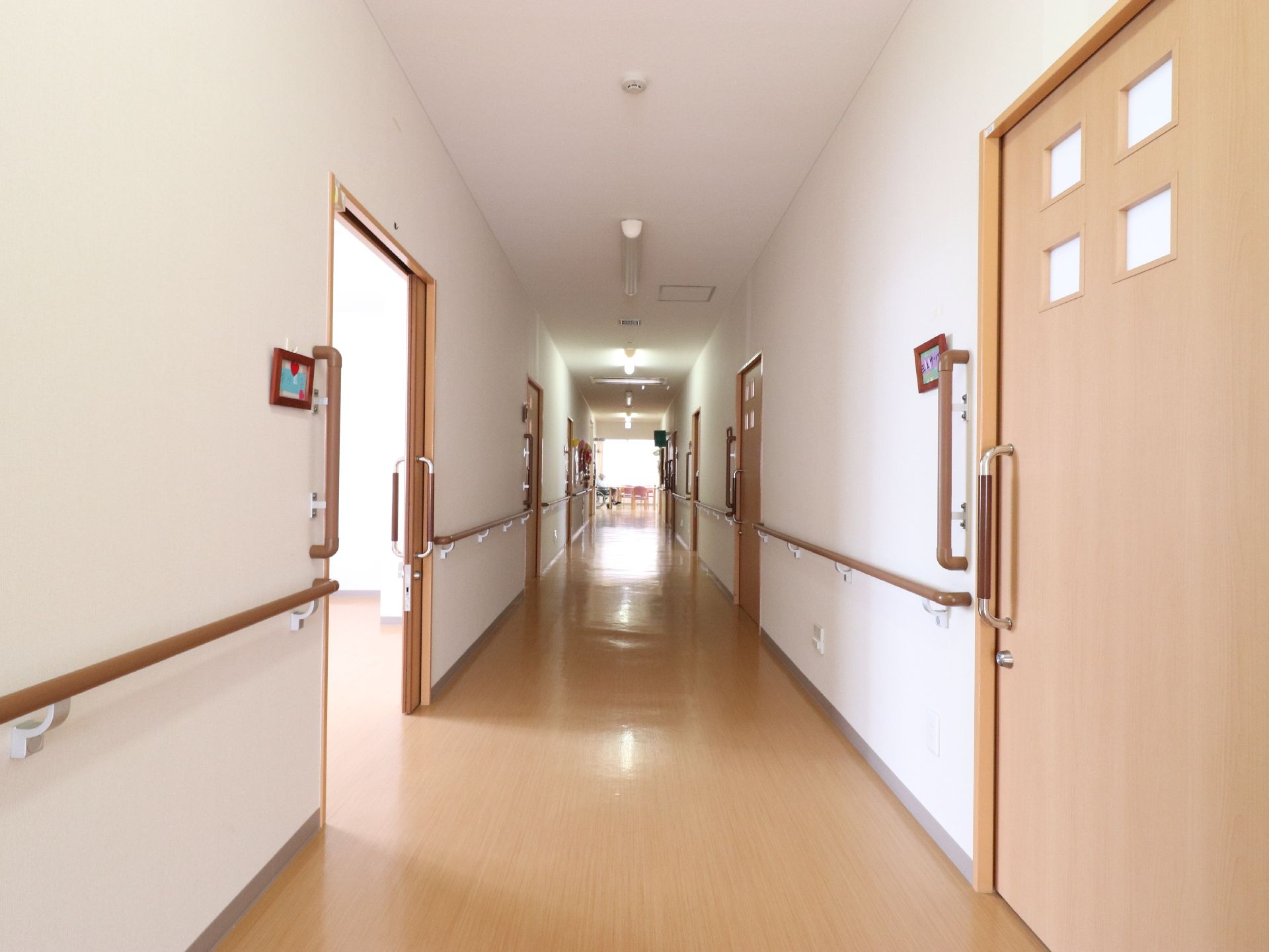 バリアフリー構造の明るい廊下の両側に、居室のドアが連なっている。床面とドア、また手すりの木質はマッチしており、こだわりがうかがえる。