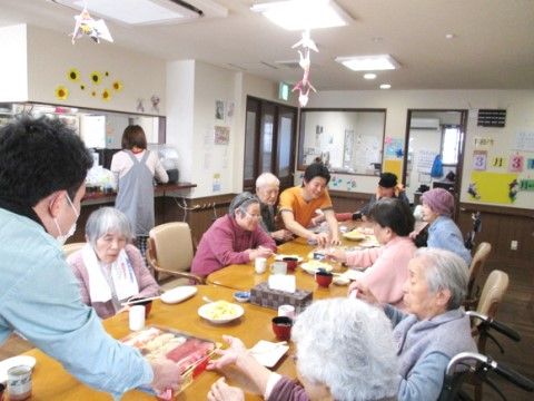 食堂に集まってスタッフのサポートの下、お食事を召し上がろうとしている入居者様達