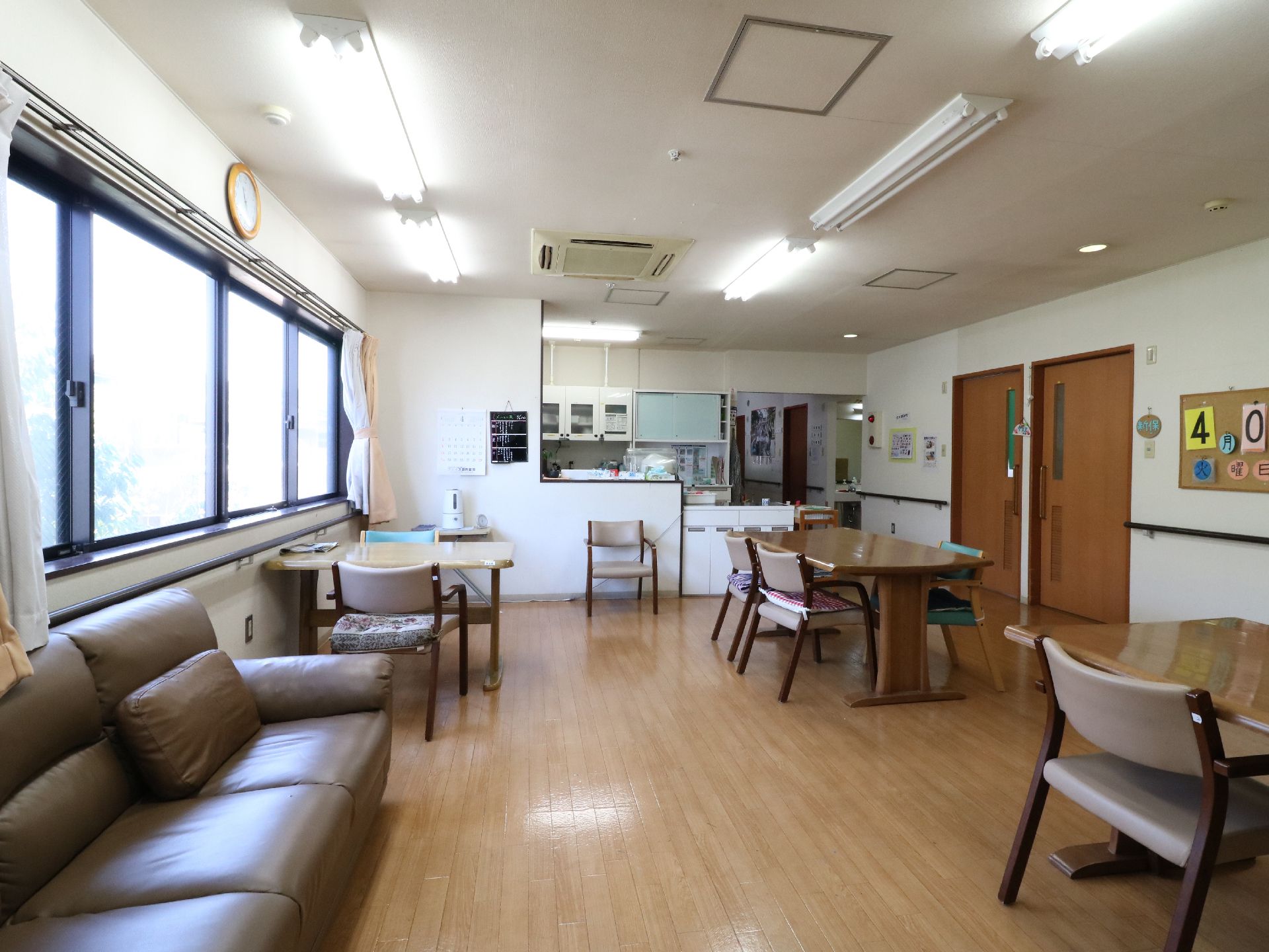 食堂にはテーブルと椅子、ソファーなどが置かれていて奥にはキッチンが見える。キッチンの奥は廊下が続いているのが見える。