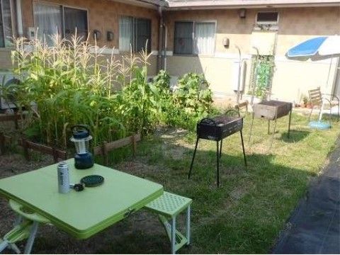 夕暮れ時の中庭である。バーベキューコンロが２つ用意され、椅子やテーブルが置かれている。蚊取り線香やランプも見える。