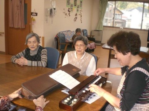 テーブルの上に置かれた楽器を演奏している女性とそれを聴いている入居者様たち