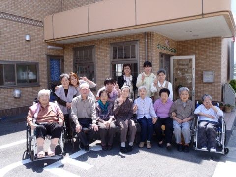 玄関前に集合して、ピースサインをしたり笑ったりしながら写真に収まっている入居者様とスタッフ