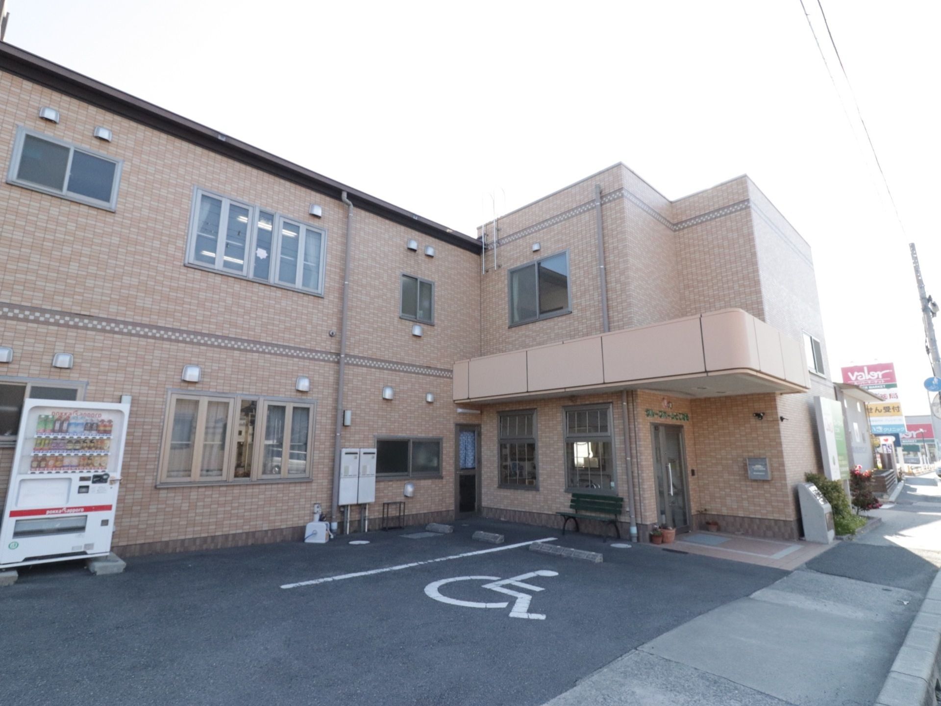 2階建のモダンな建物である。エントランスの前に車椅子専用駐車場が完備されていて便利である。自動販売機もある。