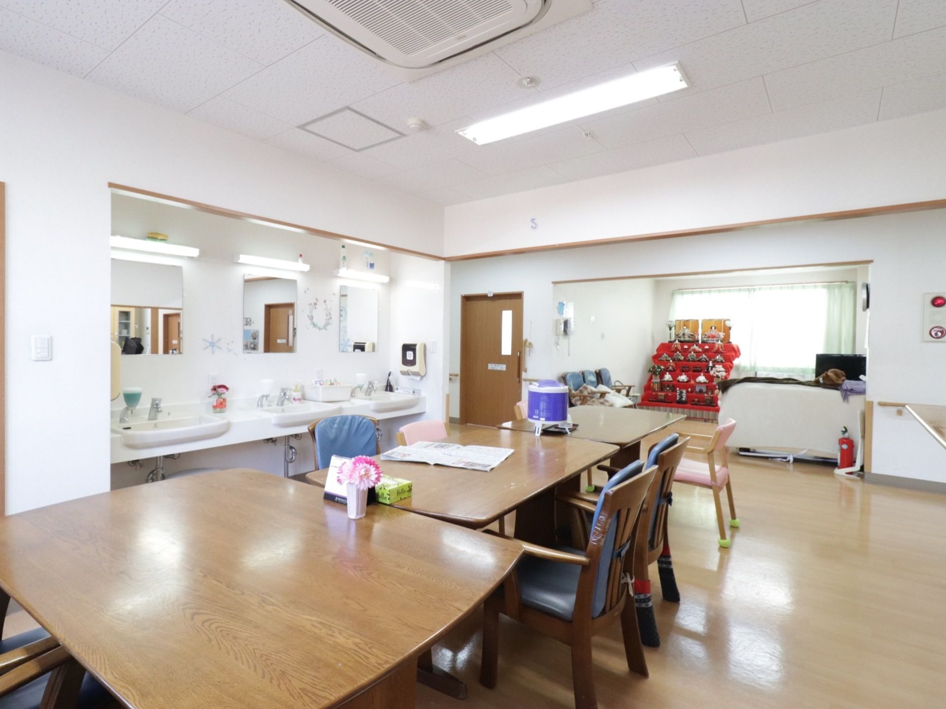 開放的な食堂で洗面台も3つ設置してある。バリアフリーで隣の共有スペースには大きいソファーや季節を感じる部屋飾りがある。