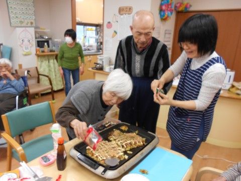 「愛の家グループホーム おおはる」のレクリエーション。ご入居者様とスタッフが一緒にお好み焼きを作っている。