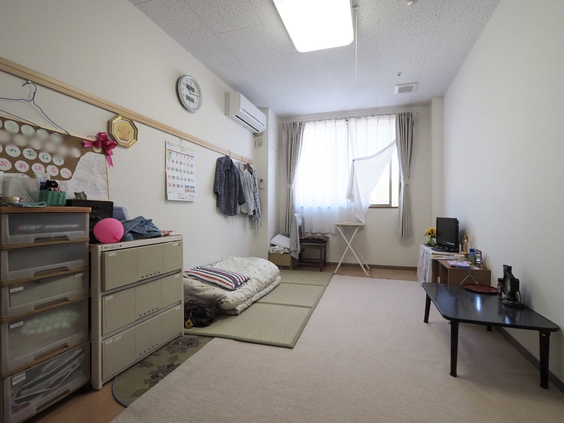 居室は奥行きのある洋室タイプ。絨毯が敷かれていて茣蓙やテーブルタンス、テレビなどの備品が取り揃えられている。