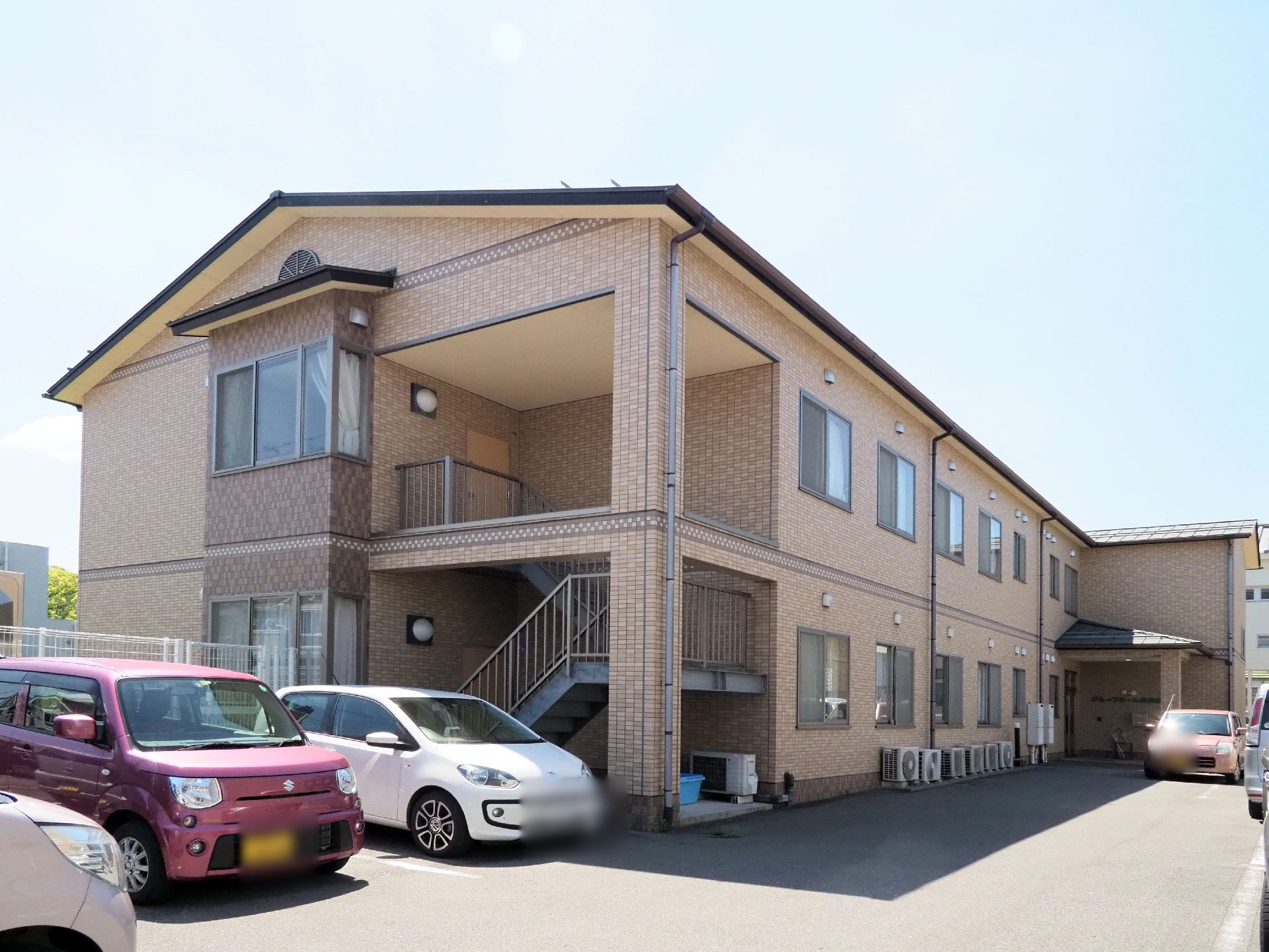 施設はレンガ調で茶色の外壁の2階建ての建物。洋館風な佇まい。敷地内には駐車場もあり車が多数停められているのが写っている。
