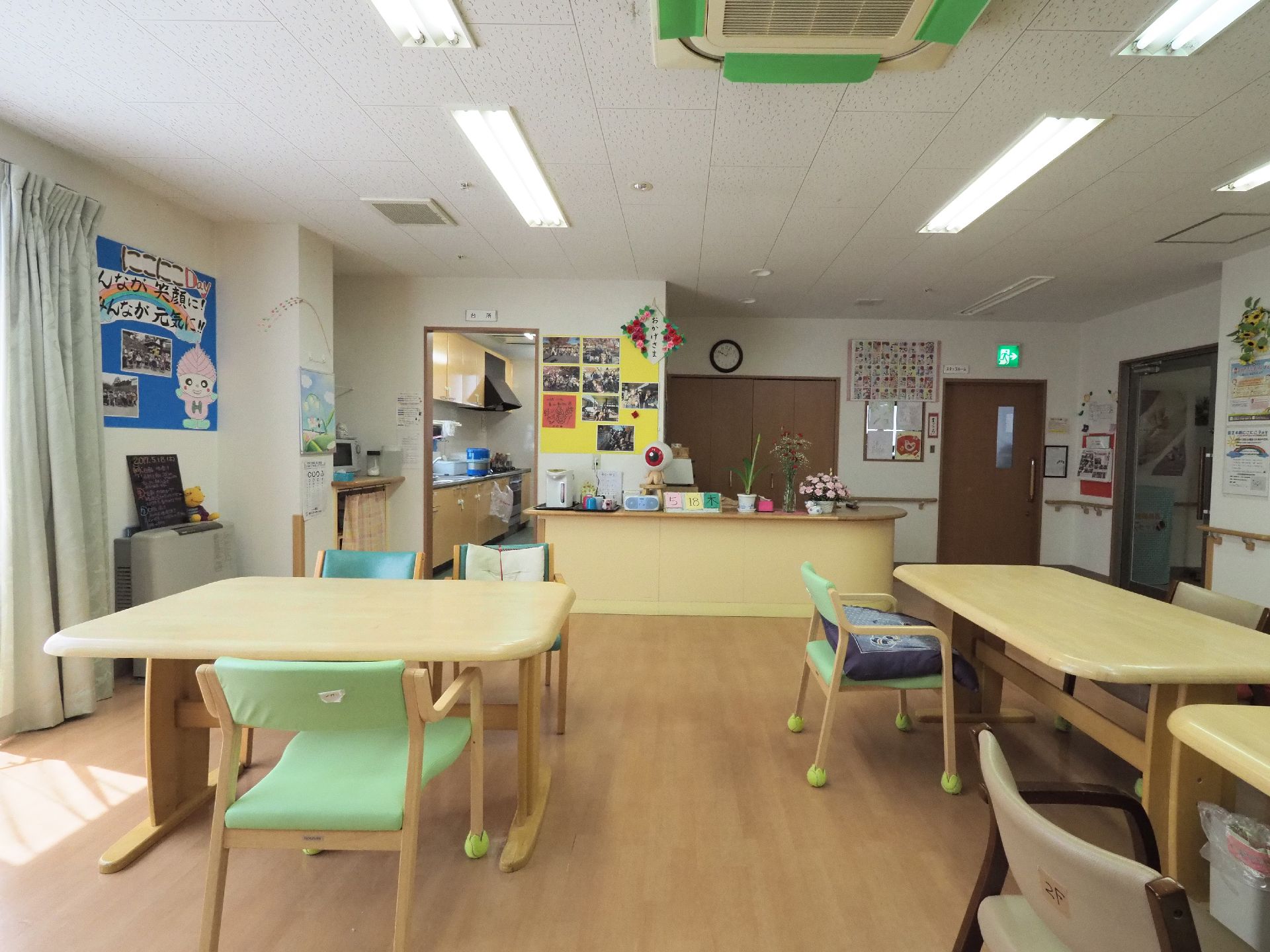 リビングは白壁にフローリングの広間。テーブルと椅子が置かれていて天井にはエアコンがある。カウンターにはポットや小物などが置かれている。