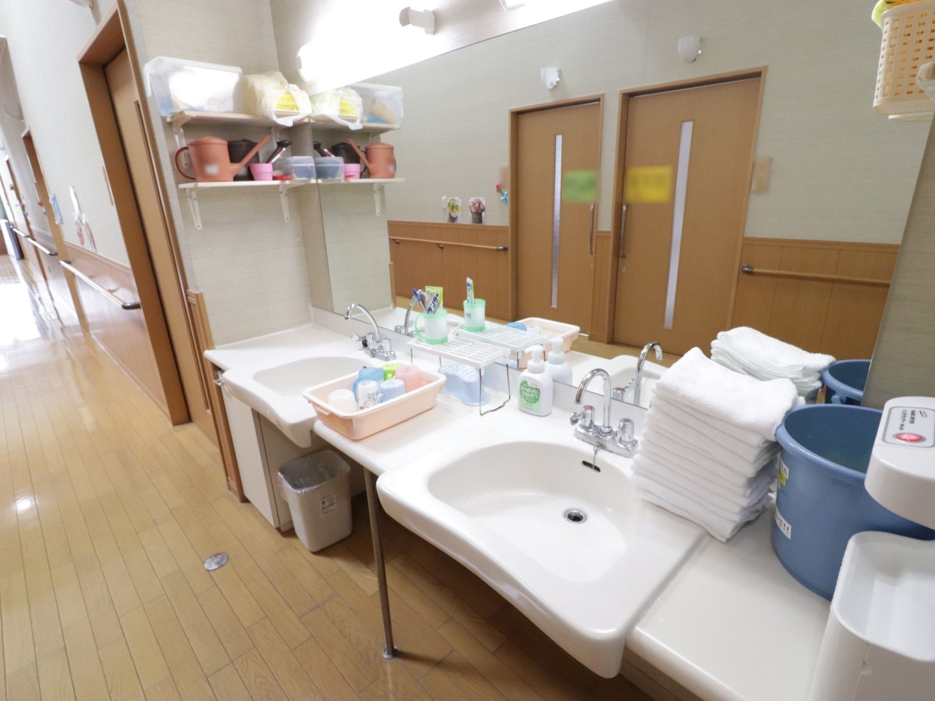 大きな白い洗面台が設置されている。洗面ボウルが２つあり、大きな鏡、照明が付いている。横の壁には収納棚が取り付けられている。