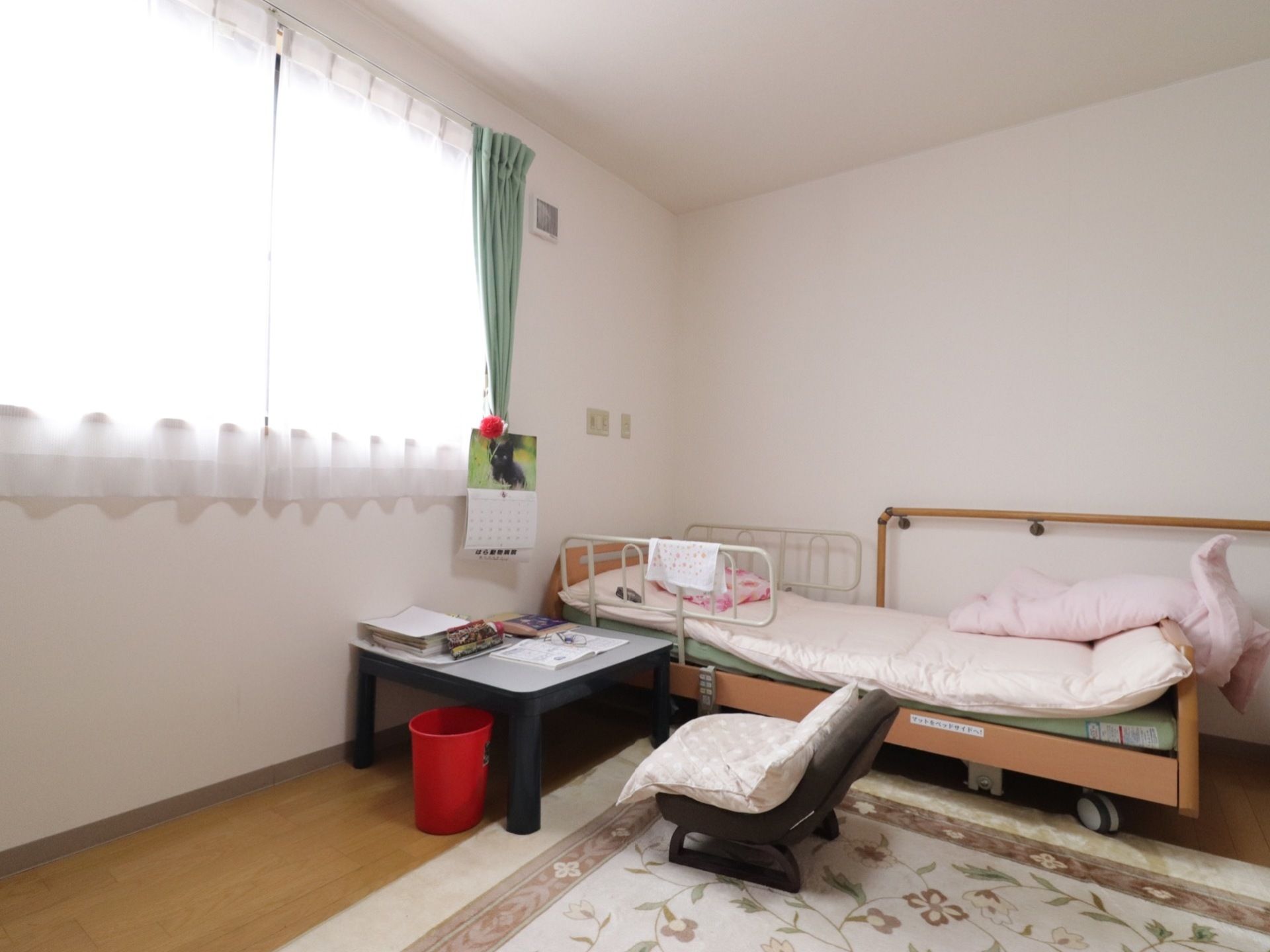 居室はゆったり広々としていて、ベッドとテーブル、座椅子が置かれている。床にはラグマットが敷かれている。