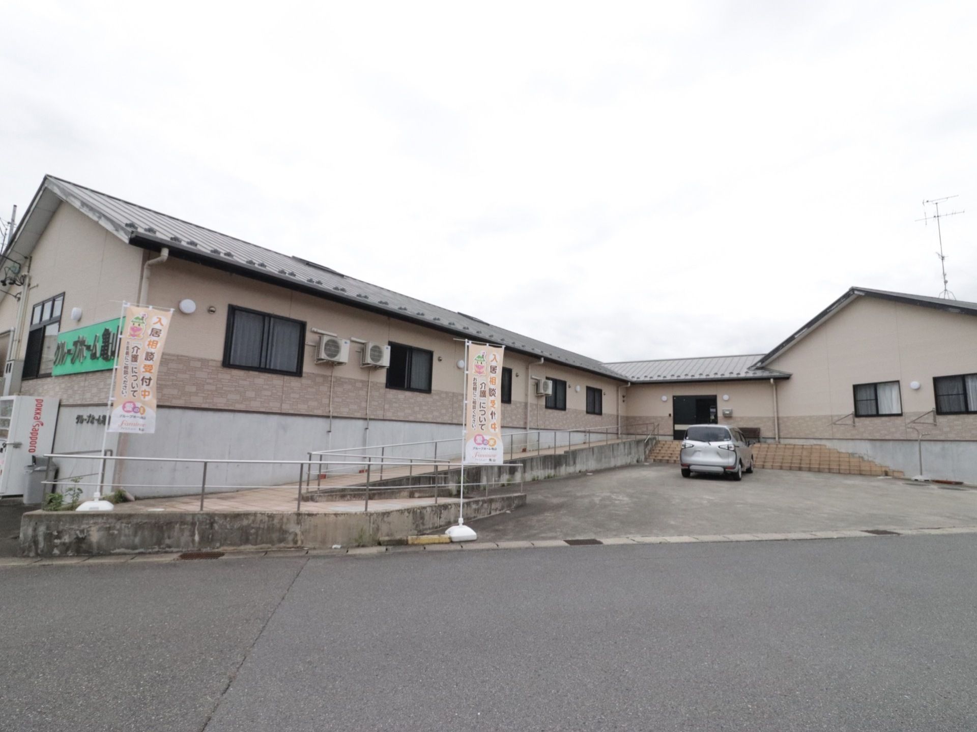 外壁には緑色の大きな看板が取り付けられ、建物の前にはのぼりが立っている。入り口までスロープと手すりが設置されている。