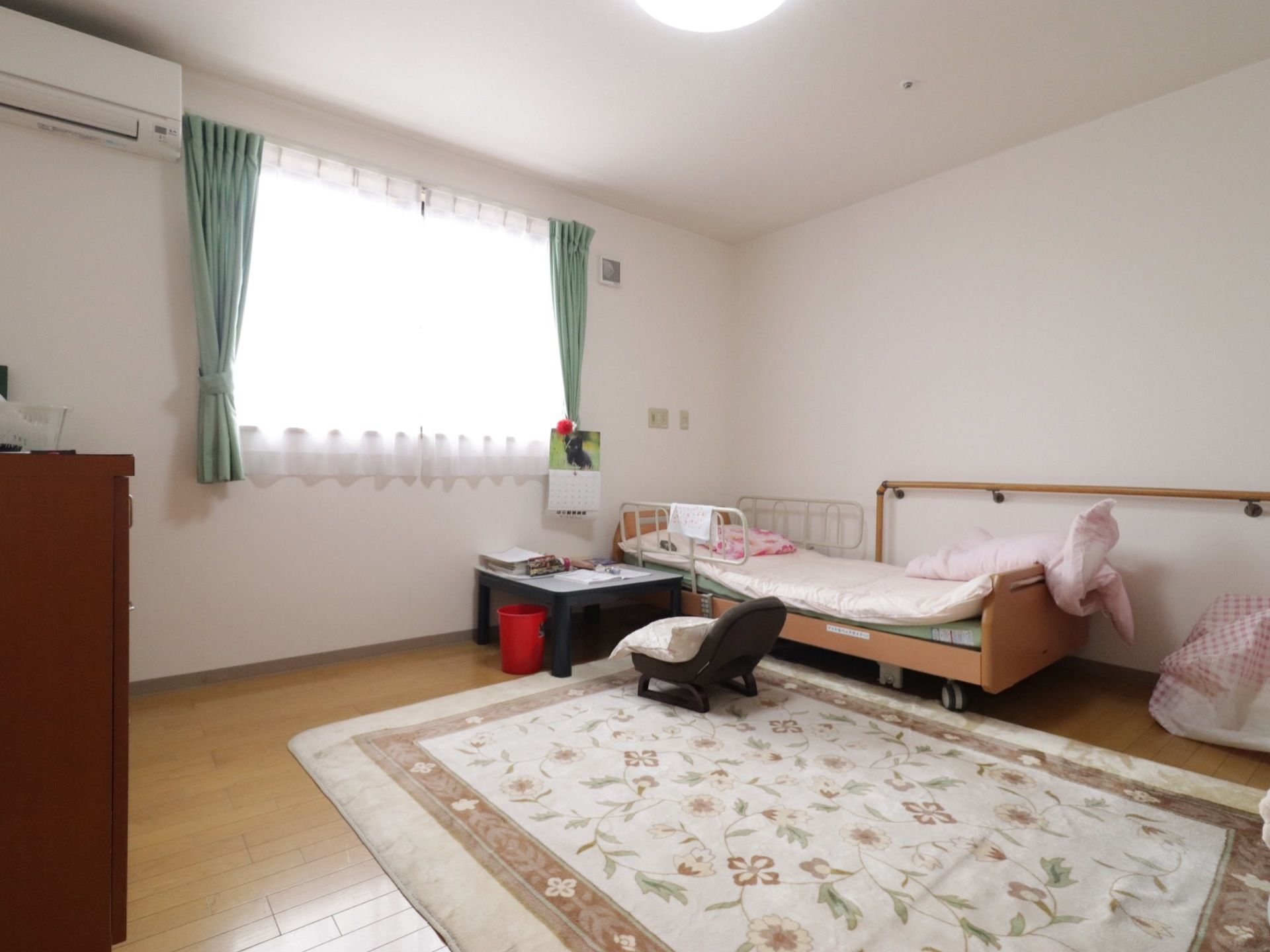 居室は広く、介護ベッドや家具を置いても十分な広さがある。ベッドと家具に間には、ベージュの花柄の絨毯が敷いてある。