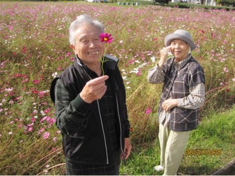 季節の花が咲いている花畑をバックに笑顔の男女の入居者様