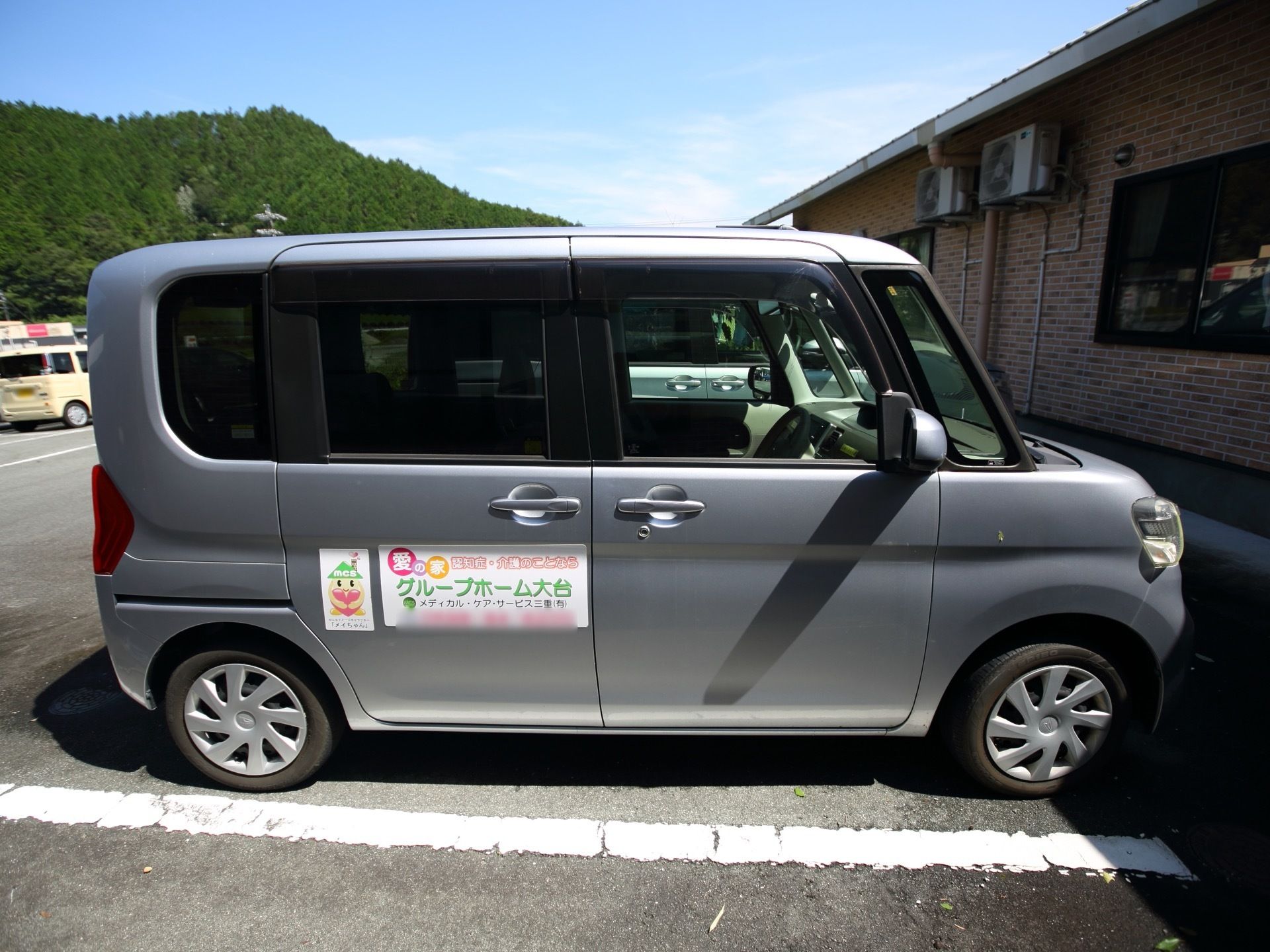 駐車場に複数台の車が停められている。一番手前の車の車体には、ホームの名称やイラストなどが書かれたシールが貼られているのが見える。