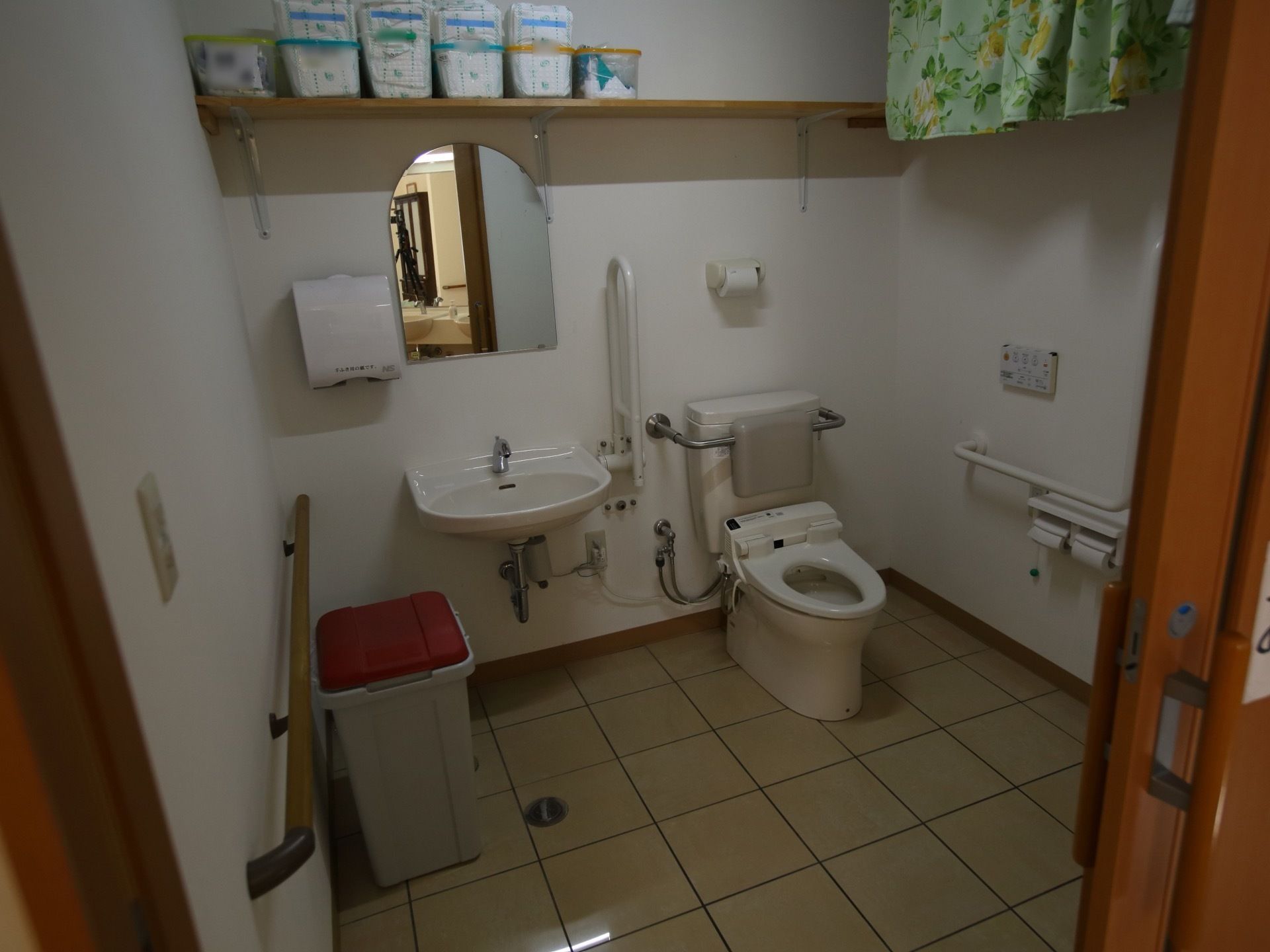 バリアフリーのトイレの個室。入口の扉は引き戸になっていて、個室内の壁には手すりが備えられている。
