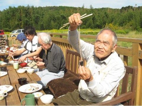 林をバックに外で食事をとっている入居者様達と男性スタッフ