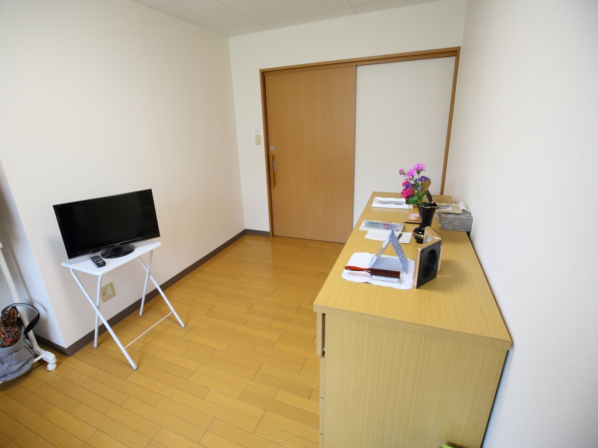 居室にはタンスが置かれ、その上には写真や花などが飾られている。扉は幅の広いスライド式である。壁と天井が白で統一されている。