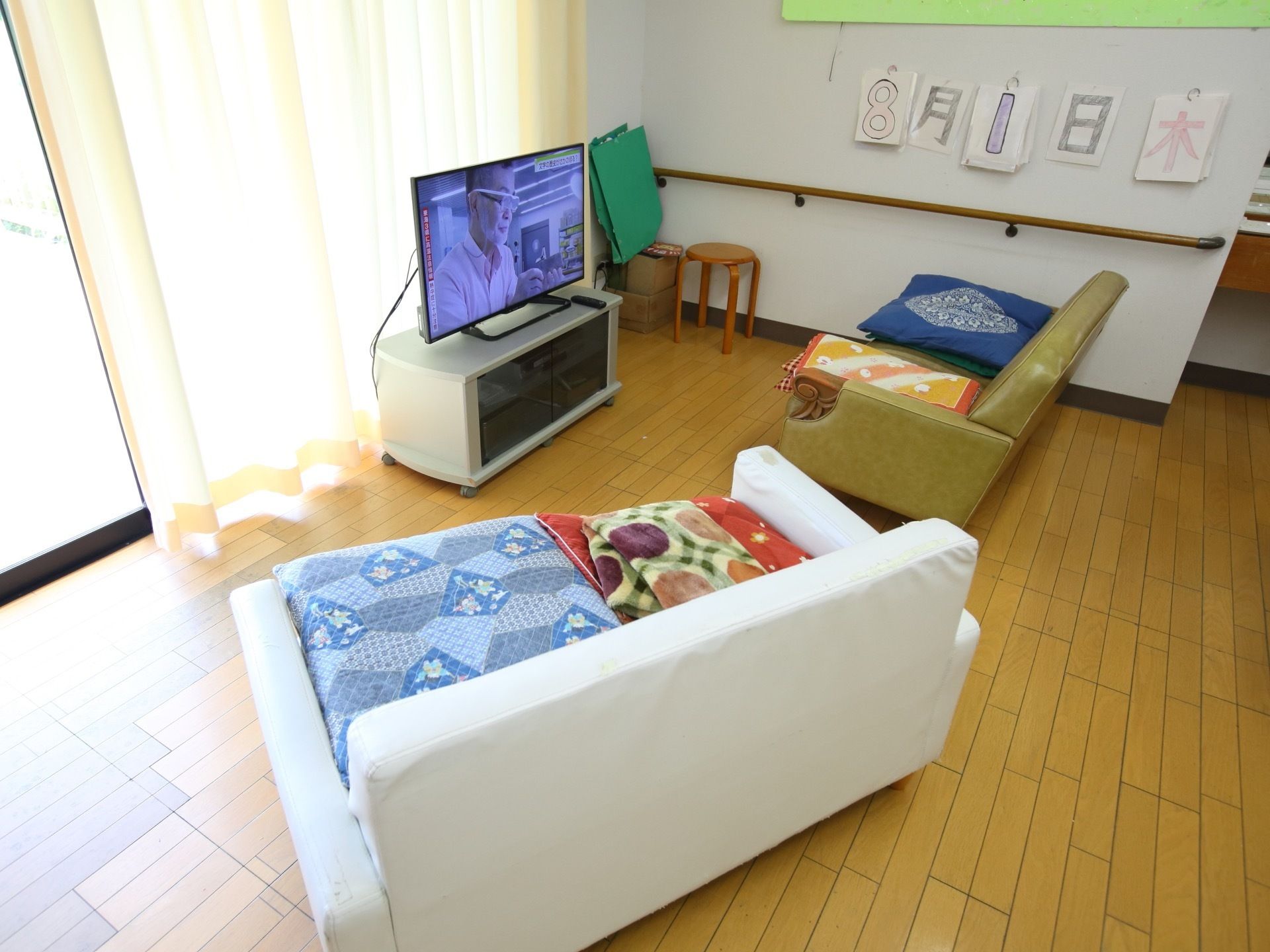 談話室には画面の大きなテレビが置かれている。大きなソファが２脚あり、くつろげるよう座布団が用意されている。