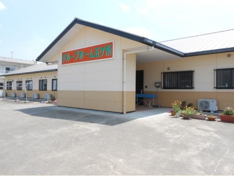 玄関前の大きな壁にある赤地の板に緑色で施設名称が書かれている看板