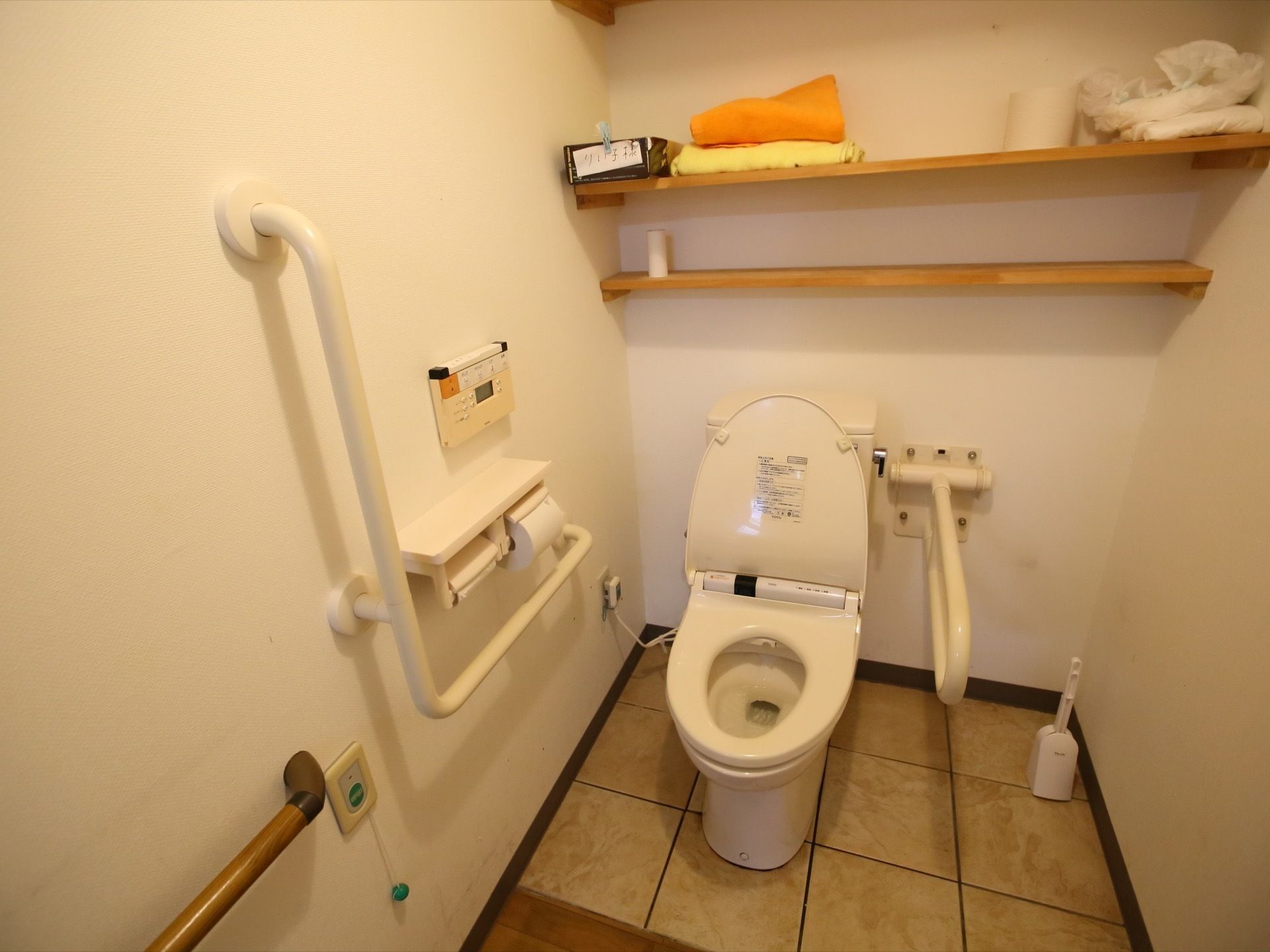 トイレに白い洋式便器が１台設置されている。便器の近くの壁には、手すりや緊急呼出し用のブザーも取り付けられている。
