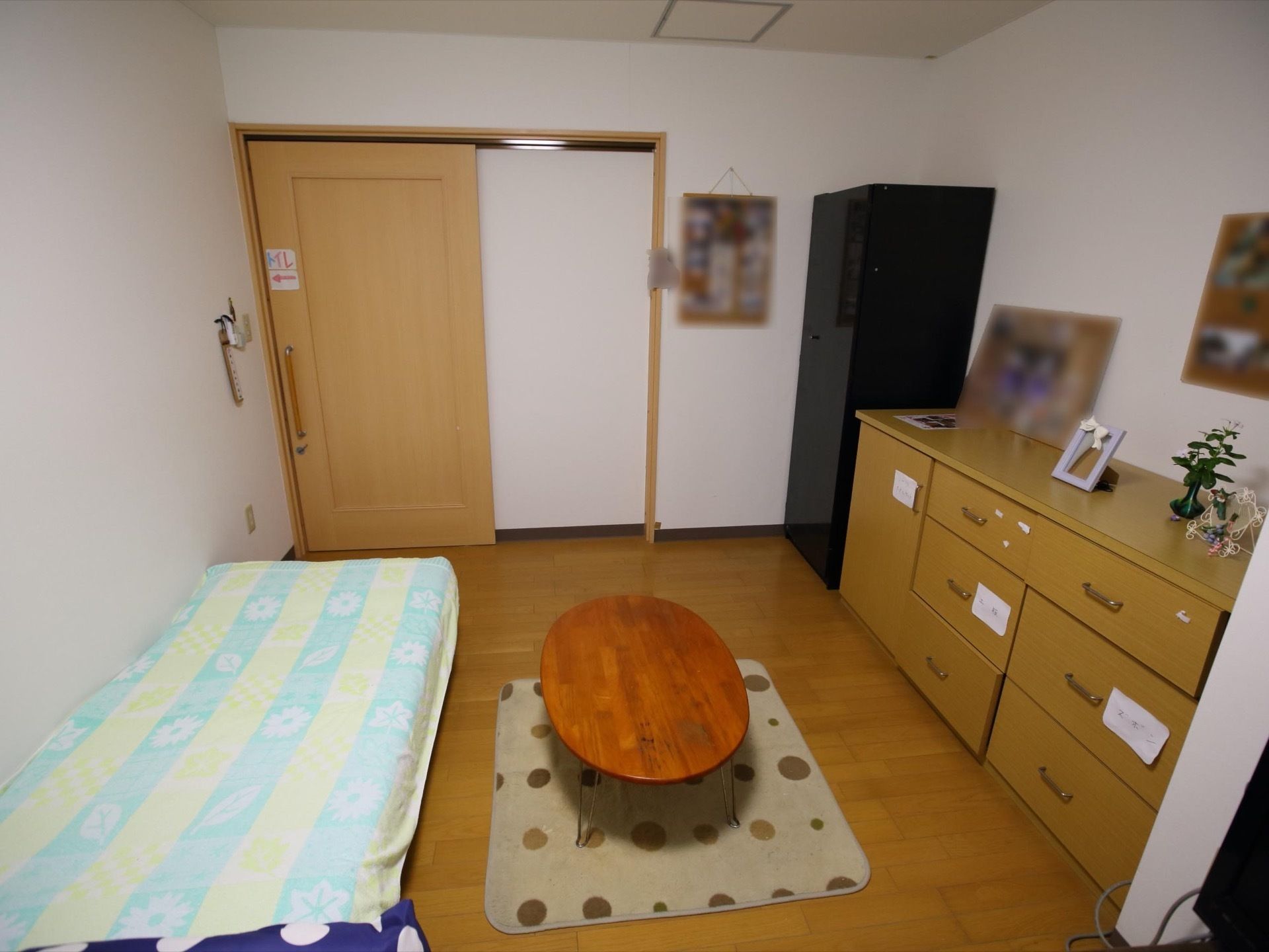 ベッド、各種の収納家具、ローテーブル、敷物などが設置されている洋風の居室。入口の扉は引き戸となっている。