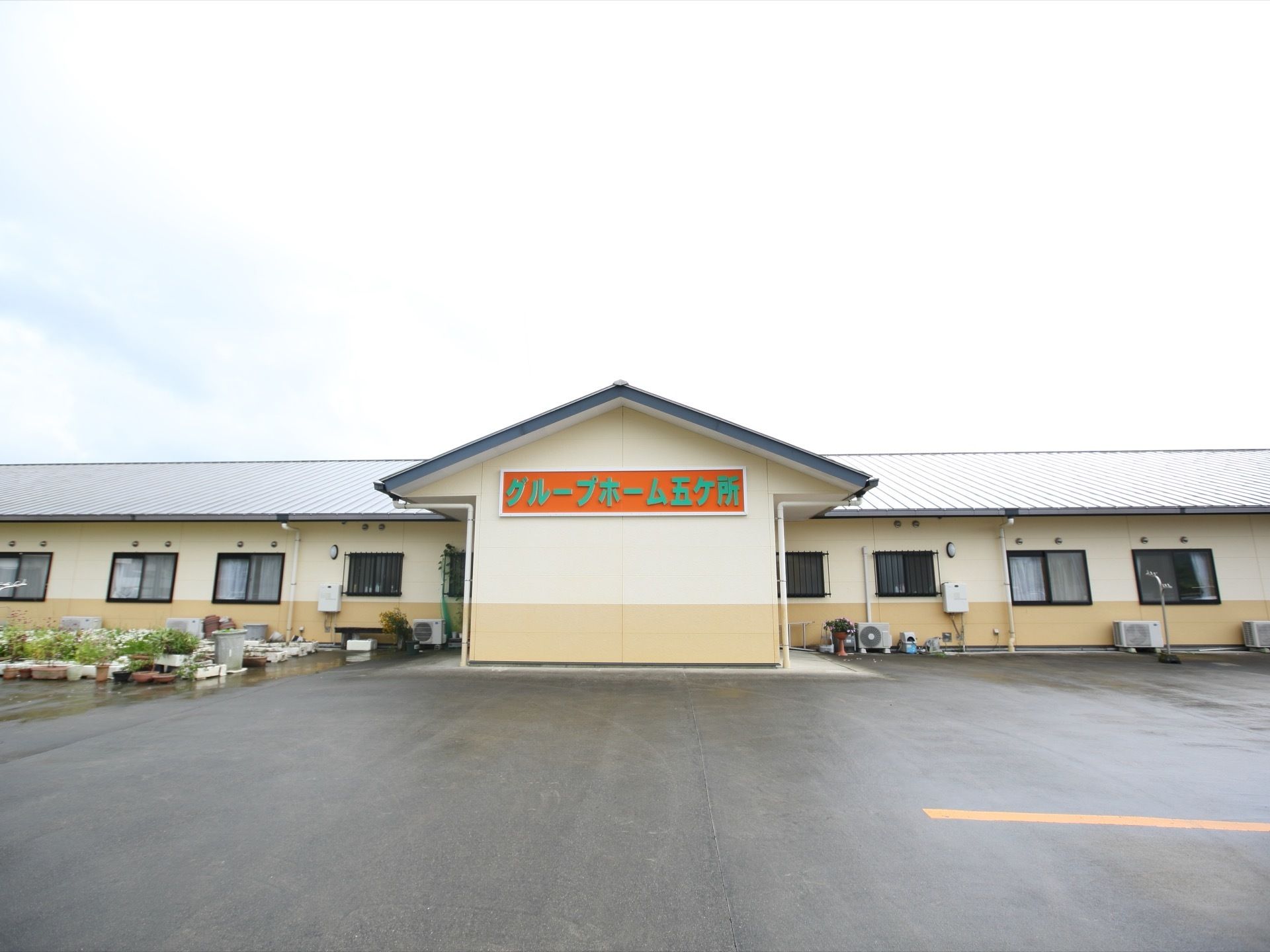 クリーム色の外壁の平屋建ての施設が正面に建っている。玄関前の壁には、施設の名称がオレンジと緑色の文字で大きく書かれている