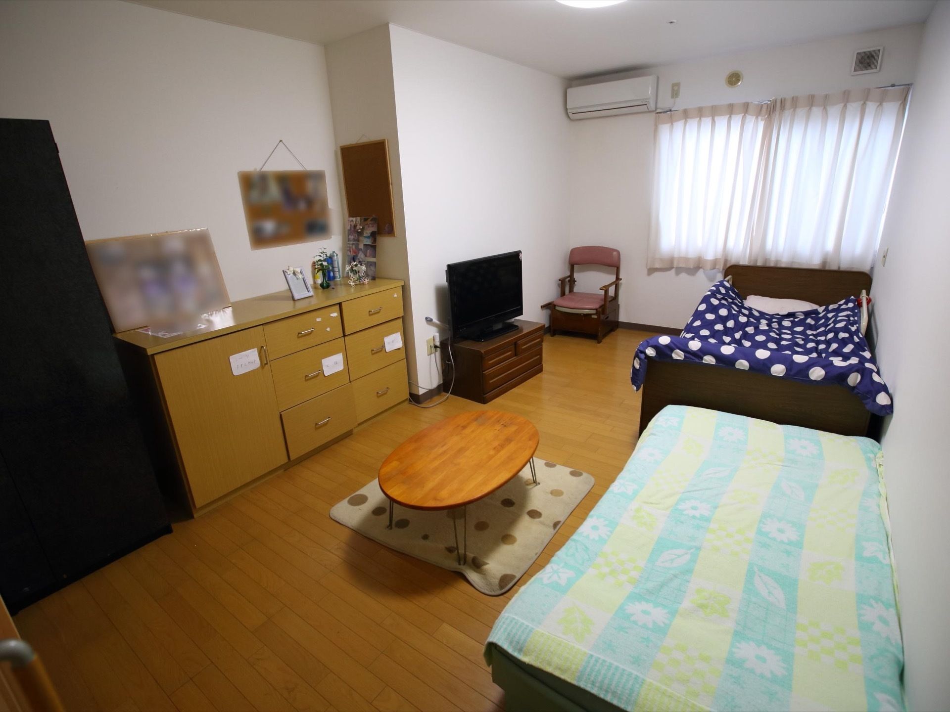 余裕のある広さの居室。エアコン、ベッド、家具調介護トイレ、テレビ、ちゃぶ台、収納タンスなどが備えられている。
