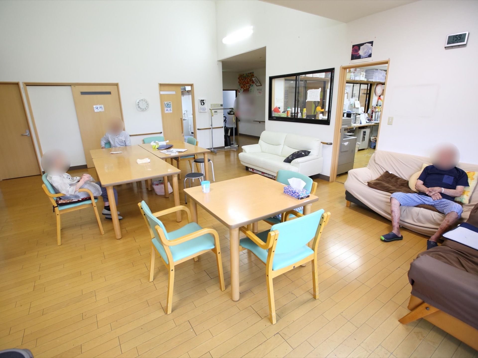 テーブルと椅子のセット、ソファ、テレビなどが並ぶ共有スペース。スペースの隣にはトイレと風呂、スタッフルームも設置されている。