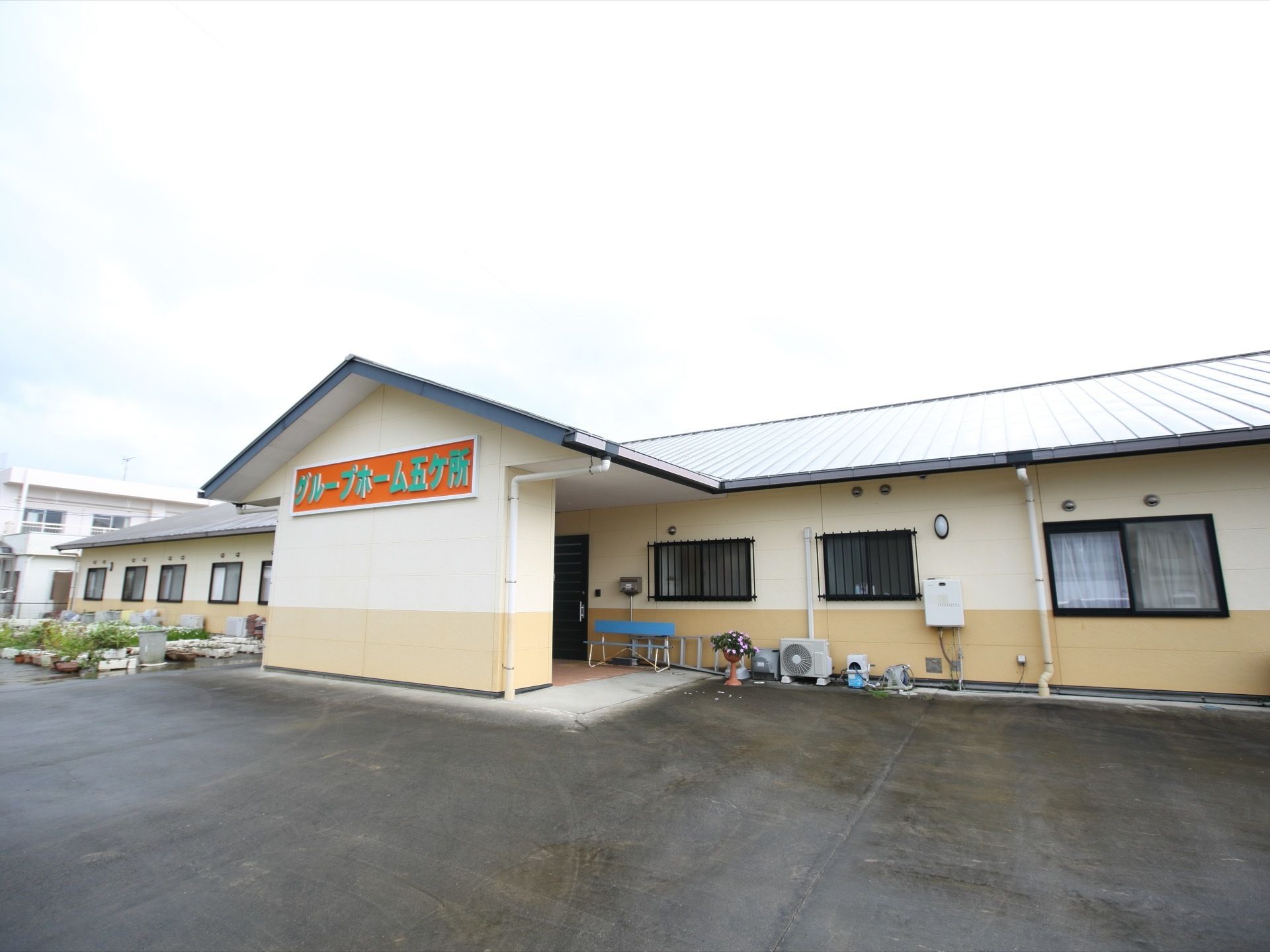 １階建ての大きな建物があり、建物の前には広い駐車場があり、たくさんの植物が植えられた鉢も置かれている。