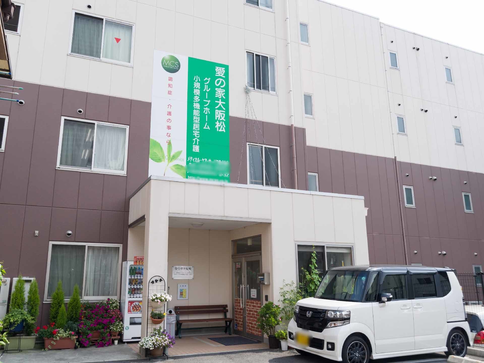 玄関前はタイルが貼ってある。駐車場はコンクリートになっていて、黒いフェンスで囲ってある。プランターがたくさんある。