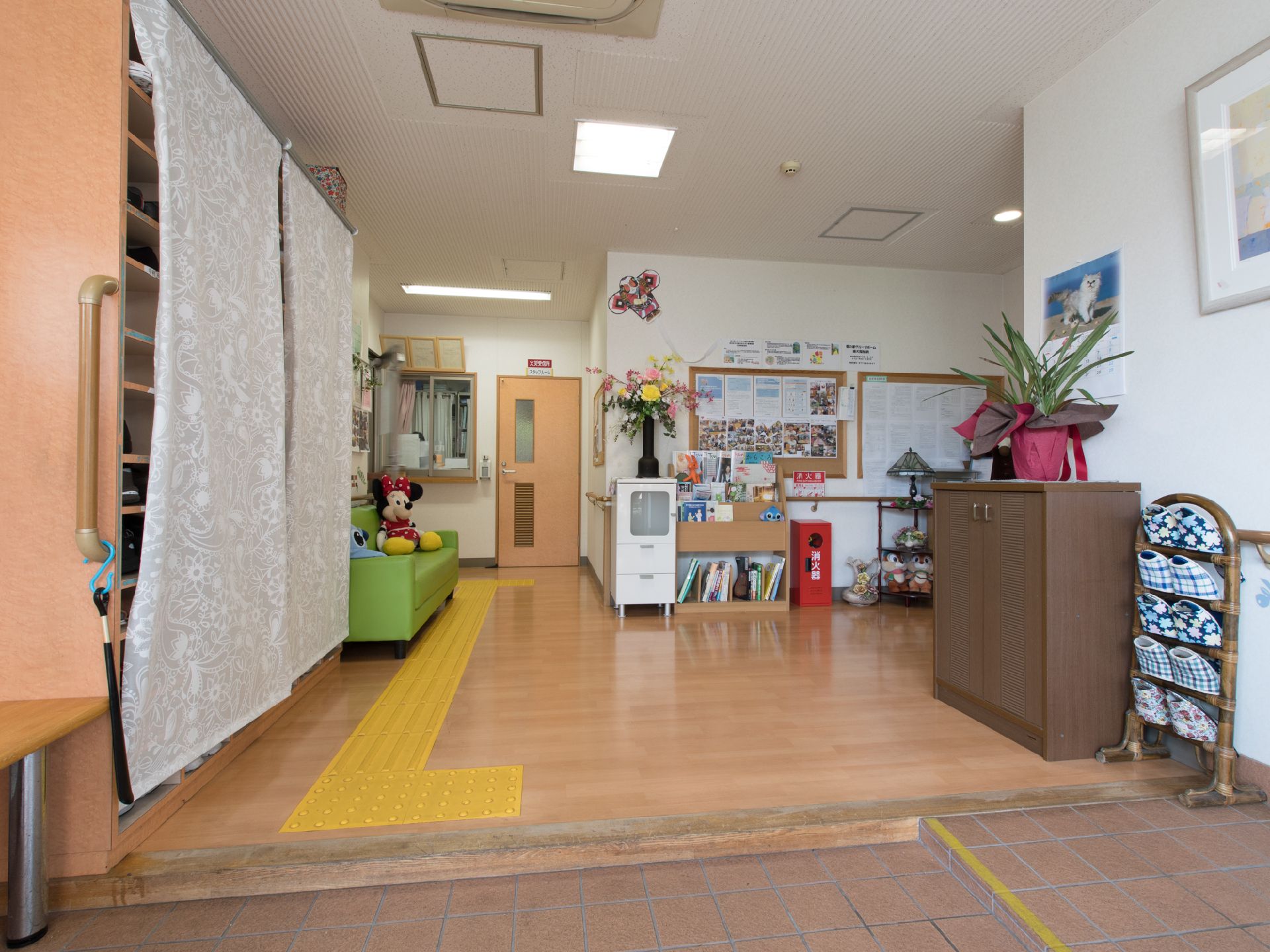 点字ブロックがある。シューズボックスにも手すりがついている。緑色のソファが置いてある。奴凧が天井近くに飾ってある。
