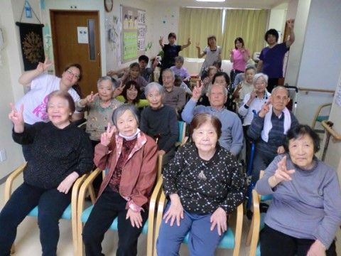 並べた椅子に座って集合写真に収まっている入居者様たちと、後方部で立っているスタッフ