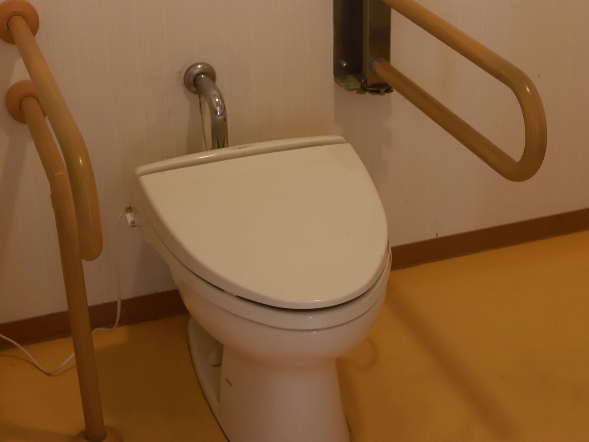 柔らかな色合いの床、壁紙が清潔に保たれている。トイレの脇には手すりが用意され、周囲にも広いスペースが確保されている。