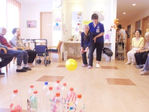 スタッフのサポートを受けながら、柔らかいボールとペットボトルでボーリングを楽しんでいる入居者様たち