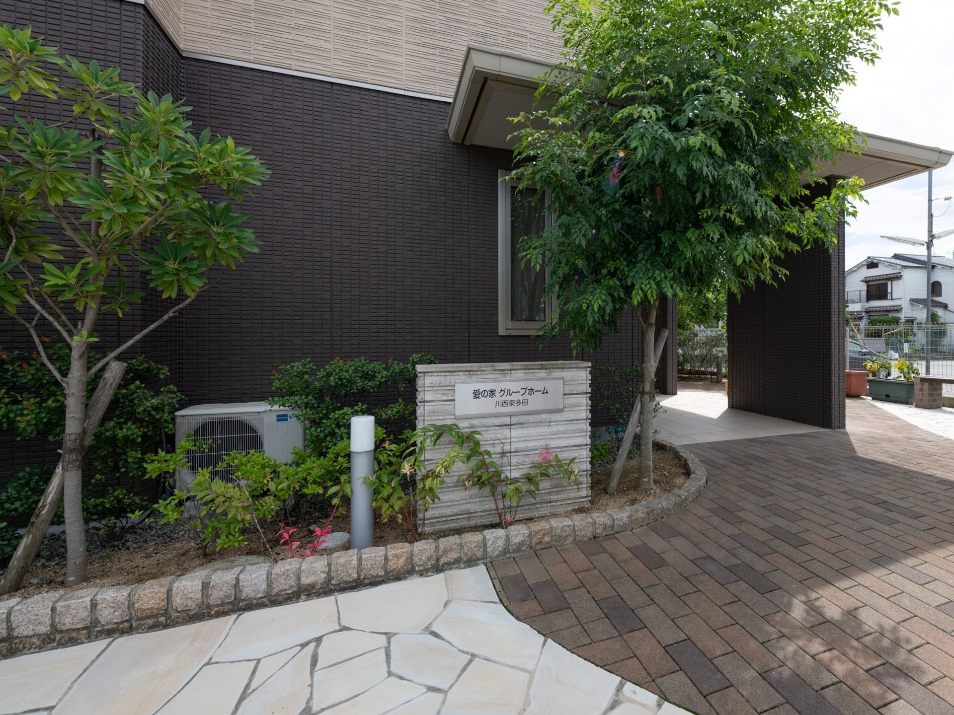 エントランスは玄関アプローチまで、緩い勾配になっている。建物の壁際には、庭木が植えられた花壇が設けられている。