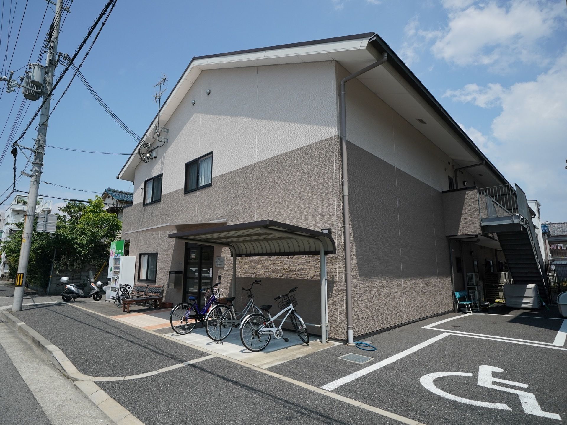2トーンで施工された、落ち着いた色合いの建物である。屋根がついた駐輪場が完備されている。そばには車椅子専用駐車場もある。