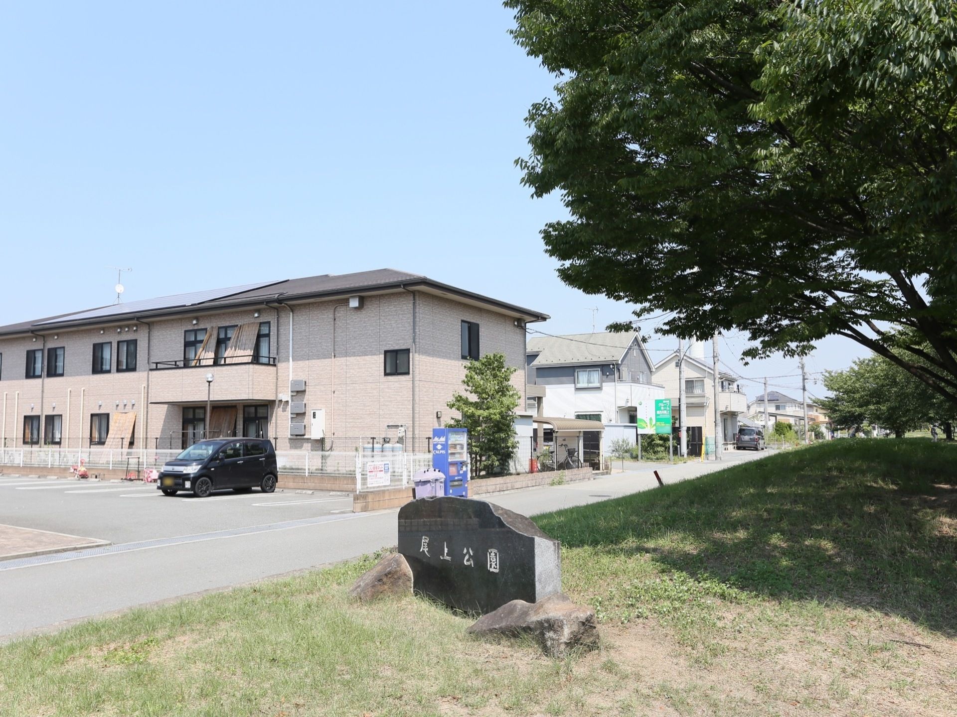 施設の近くに、何本かの大きな木が生えている緑豊かな公園がある。低層の建物が多いのどかな地区に立地している。