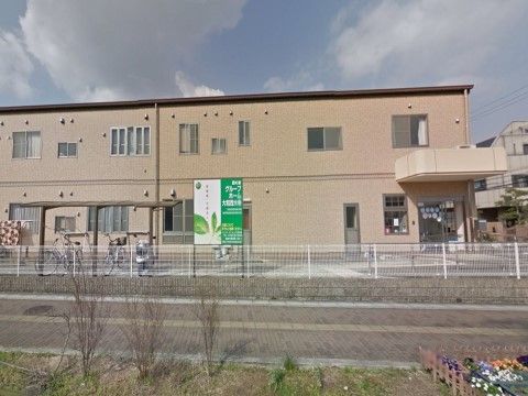 道路沿いの敷地境界に白色のフェンスが立っている、道路越しの施設外観