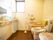 ダークブラウンの木目調の床で、広いトイレがある。小窓が付いていて明るい。洗面台があり、壁と便器には手すりが付いている。