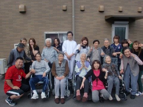 施設建物の前に集まって集合写真に収まっている入居者様たちとスタッフ