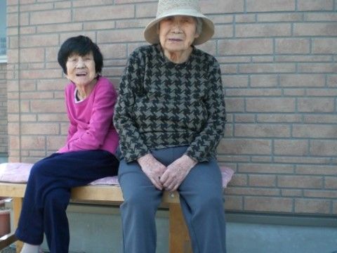外に置かれたベンチに座ってカメラの方を見ている２名の女性入居者様