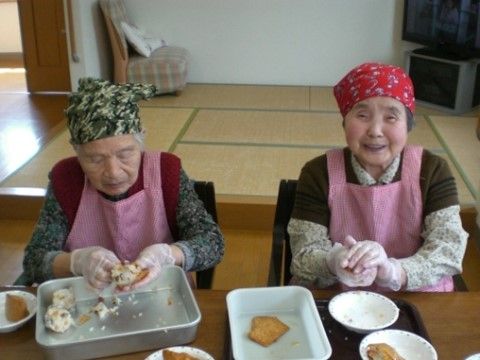 エプロンをして、椅子に座りながらおかずづくりをしている２名の女性入居者様