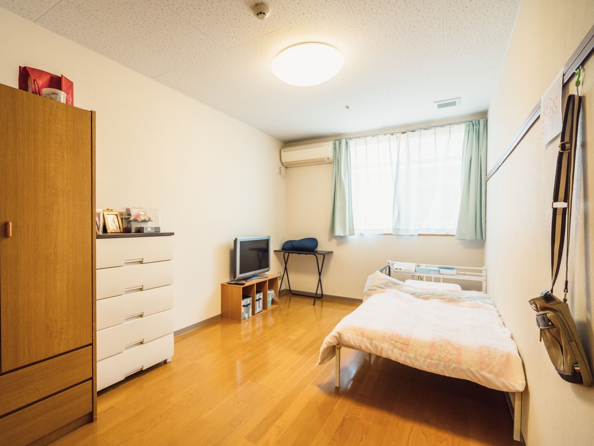 居室にはタンスや衣装ケース、テレビが置かれており、写真や雑貨が飾られている。部屋には大きな窓があり、日の光がたっぷり差し込む。