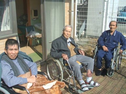 外で日光浴をしている、車いすをご利用の３名の男性入居者様