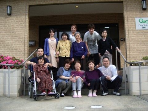 玄関前に並んで集合写真を撮っている入居者様たちとスタッフ
