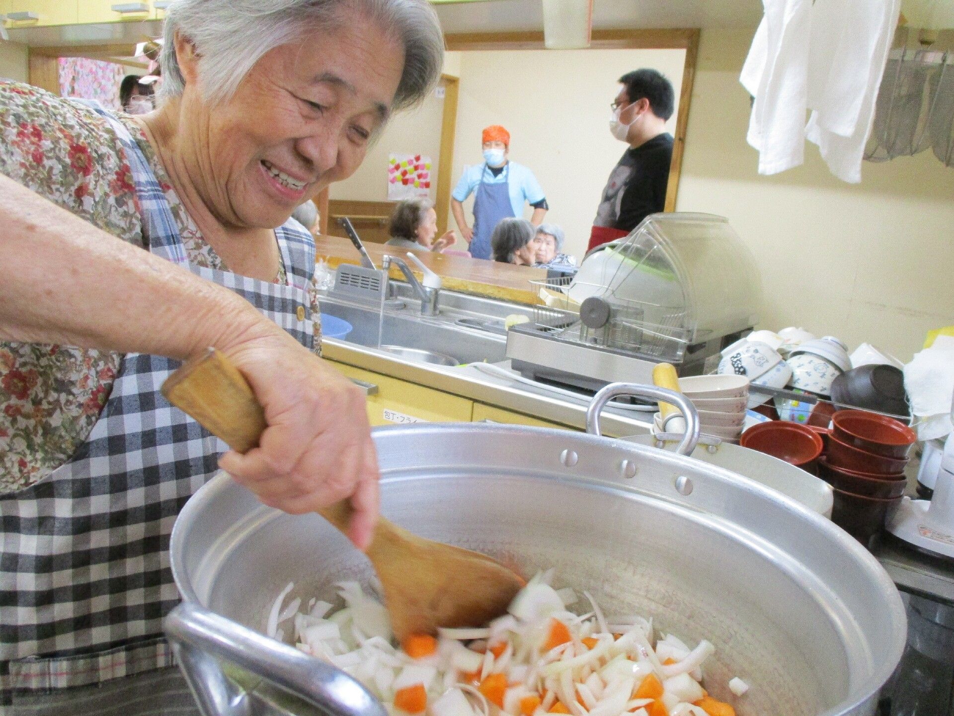 笑顔を浮かべながら、大きな鍋で野菜を炒めている女性入居者様
