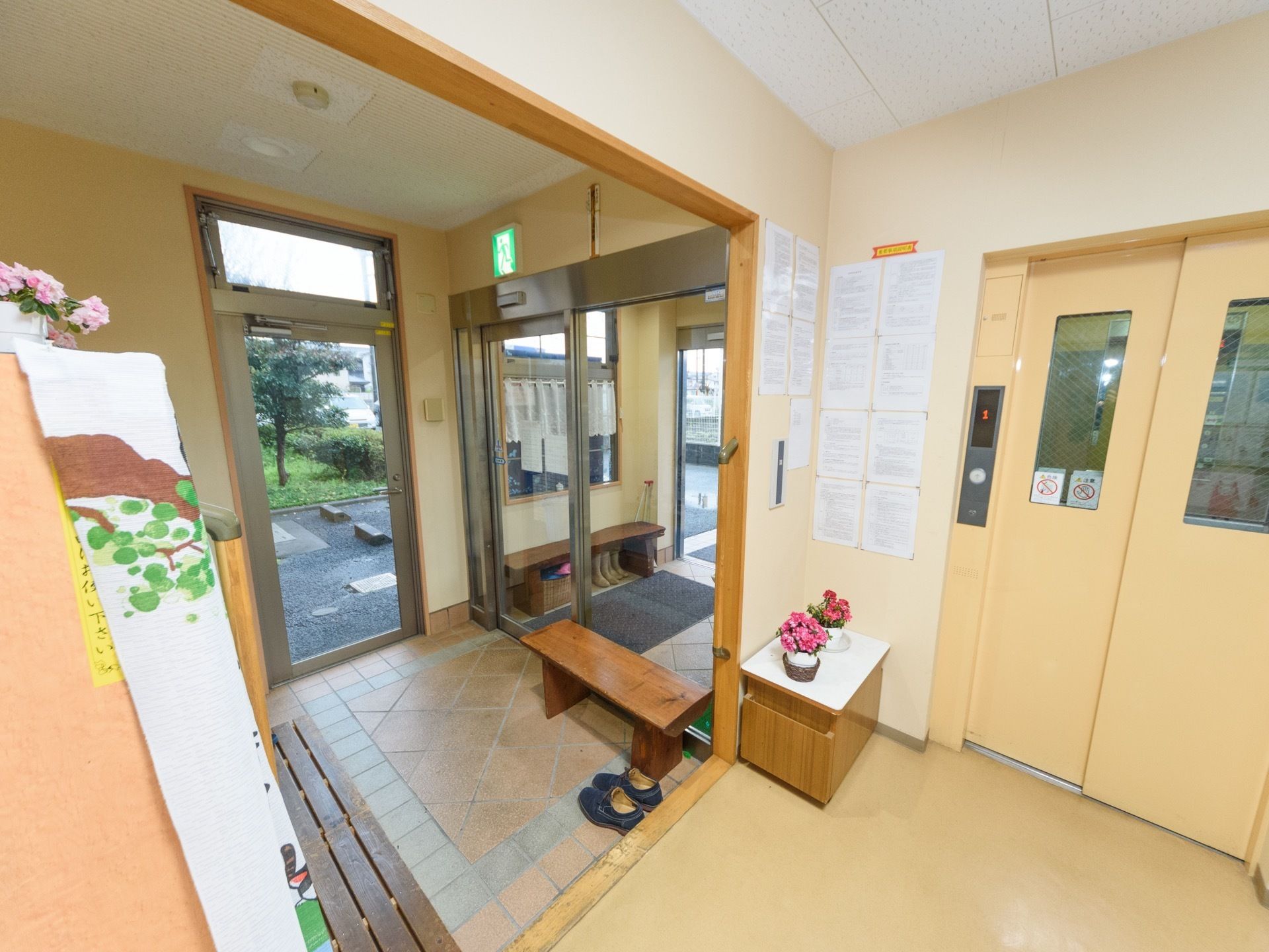 エントランスホールは広々とした空間になっている。右側にエレベーターが設置されている。自動ドアの前には、木製ベンチが置かれている。