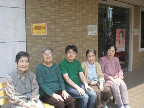 玄関前にあるベンチに並んで座って写真に収まっている入居者様たちとスタッフ