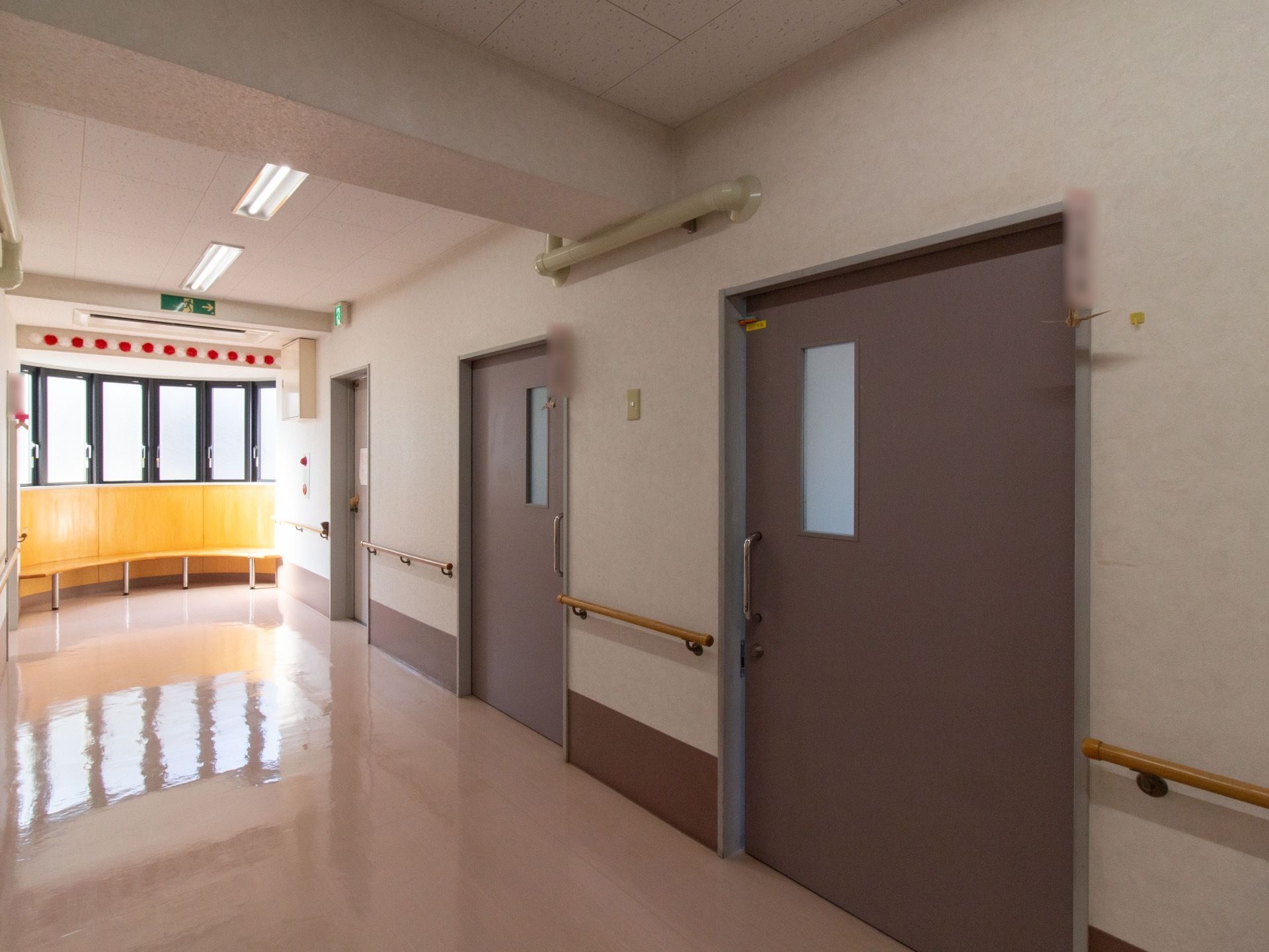 壁には大きなグレーの引き戸が並んでいる。通路の奥には窓があり明るく、壁に沿ってベンチが設置されている。