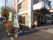 建物の前にはのぼりや看板がある。玄関の上には屋根がついており、自動販売機やベンチなどが置かれている。